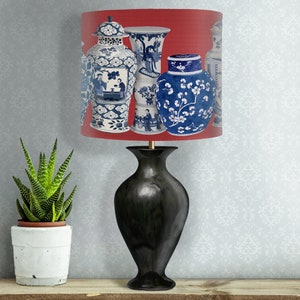 May include: A black lamp with a red and white lampshade featuring a pattern of blue and white porcelain vases. The vases have floral and geometric designs.
