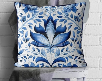 May include: Blue and white floral patterned throw pillow with a decorative design. The pillow is on a white chair with a blue and white throw blanket.