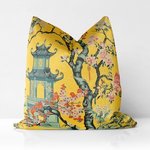 May include: Yellow cushion with an Asian-inspired design featuring a pagoda and flowering trees. The design includes teal, pink, and orange floral accents. The background is a solid yellow.
