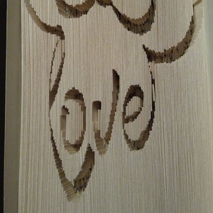 May include: A book with pages folded and cut to create a 3D design of a bow and the word "love".
