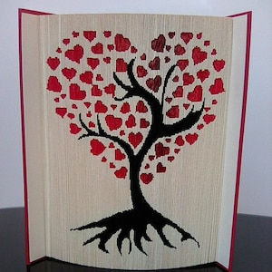 Może przedstawiać: Rzeźba z książki przedstawiająca drzewo z koroną w kształcie serca wykonaną z czerwonych serc. Drzewo ma czarny pień i korzenie.