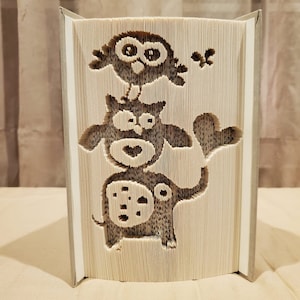 May include: A book with a 3D design of an elephant, an owl, and a bird. The design is created by folding the pages of the book.