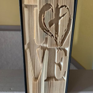 May include: A book with the word "love" folded into the pages. The book is bound in black and the pages are a light brown color.