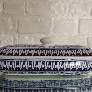 May include: A ceramic serving dish with a lid, featuring a blue and white floral pattern. The oval-shaped dish has a matching lid with a small knob. The design includes intricate details and a symmetrical arrangement, suitable for kitchen decor.