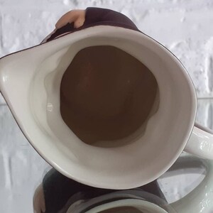 May include: A white ceramic pitcher with a brown interior and a dark brown rim. The pitcher has a handle and a spout. The image is taken from above, showing the inside of the pitcher.
