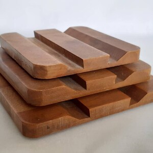 Puede incluir: Una pila de cuatro jaboneras de madera, cada una de un tama&ntilde;o diferente, en un tono marr&oacute;n c&aacute;lido. Las jaboneras tienen forma rectangular con un borde curvo y un dise&ntilde;o ranurado para el drenaje. La disposici&oacute;n crea un efecto escalonado.