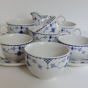 May include: A white porcelain tea set with blue floral patterns. The set includes teacups, saucers, a creamer, and a sugar bowl. The cups have handles and the rims are scalloped. The blue design features flowers and leaves.
