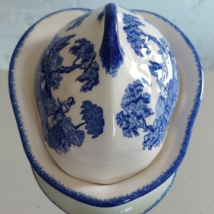 May include: A white and blue ceramic serving dish with a lid. The lid and dish feature a blue and white pastoral scene. The dish has a heart shape with a blue trim. The lid has a handle.