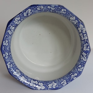 May include: White ceramic bowl with a blue and white leaf and vine pattern around the rim. The bowl has an octagonal shape and a smooth, glossy finish. The interior is plain white.