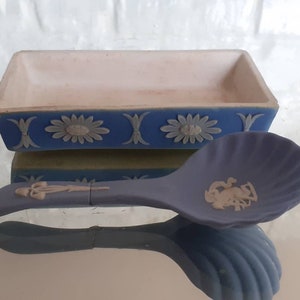May include: A blue and white ceramic dish and spoon set. The rectangular dish has a white interior and blue exterior with floral and decorative accents. The spoon is blue with a shell-shaped bowl and a decorative emblem.