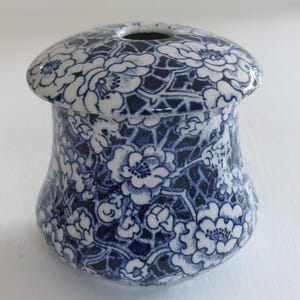 May include: A blue and white ceramic bud vase with a floral pattern. The vase has a rounded body and a lid with a single hole. The floral design is in white against a blue background.