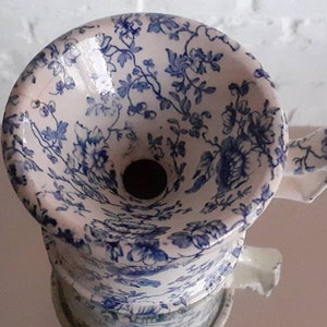 May include: A vintage white and blue floral patterned ceramic funnel. The funnel features a detailed blue floral design against a white background. The funnel has a wide top and a narrow spout, with a small handle on the side.