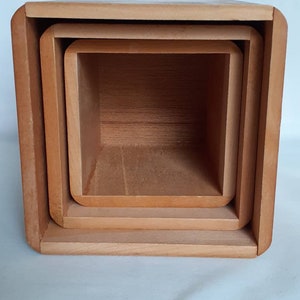 Puede incluir: Un juego de tres cajas de madera anidadas. Las cajas son cuadradas con esquinas redondeadas y est&aacute;n hechas de madera de color claro. Las cajas est&aacute;n anidadas unas dentro de otras, con la caja m&aacute;s grande en el exterior y la m&aacute;s peque&ntilde;a en el interior.