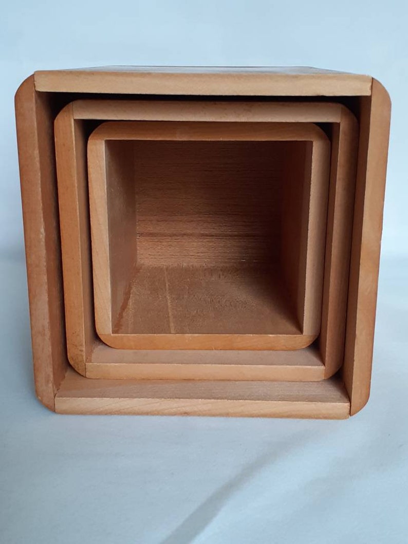 Puede incluir: Un juego de tres cajas de madera anidadas. Las cajas son cuadradas con esquinas redondeadas y est&aacute;n hechas de madera de color claro. Las cajas est&aacute;n anidadas unas dentro de otras, con la caja m&aacute;s grande en el exterior y la m&aacute;s peque&ntilde;a en el interior.