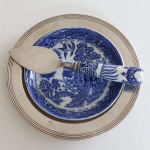 May include: A silver-plated serving plate with a blue and white patterned plate on top. A silver cake server with a blue and white handle rests on the plates. The plates and server are set against a white background.