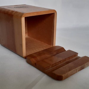 Puede incluir: Una caja rectangular de madera con tapa corredera. La caja es de madera marr&oacute;n claro y tiene un acabado liso. La tapa est&aacute; dise&ntilde;ada con tres ranuras talladas. La caja est&aacute; abierta, revelando el interior.