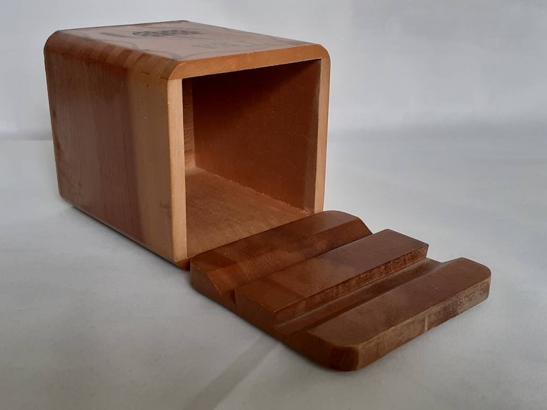 Puede incluir: Una caja rectangular de madera con tapa corredera. La caja es de madera marr&oacute;n claro y tiene un acabado liso. La tapa est&aacute; dise&ntilde;ada con tres ranuras talladas. La caja est&aacute; abierta, revelando el interior.