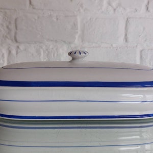 Peut inclure: Plat à servir ovale en céramique blanche avec couvercle, orné de rayures bleues. Le plat est doté d'un couvercle avec un petit bouton. Le design est simple et élégant, idéal pour servir des aliments.