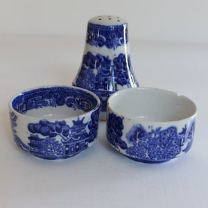 May include: A blue and white ceramic salt shaker and two small bowls. The salt shaker is tall and cylindrical with a flared base and a series of holes at the top. The bowls are round with a similar blue and white pattern.