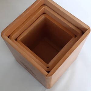 Puede incluir: Juego de cuatro cajas anidadas cuadradas de madera de diferentes tama&ntilde;os. Las cajas son de color marr&oacute;n claro y tienen un dise&ntilde;o sencillo. Las cajas est&aacute;n apiladas unas dentro de otras.