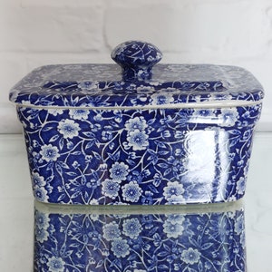 May include: A rectangular ceramic container with a lid, featuring a blue and white floral pattern. The container has a rounded knob on top of the lid. The design is a classic, vintage style, suitable for kitchen or home decor.
