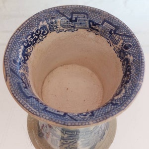 May include: A blue and white ceramic vase with a detailed pattern around the rim and base. The interior is a light beige color. The vase has a wide opening and a pedestal base.