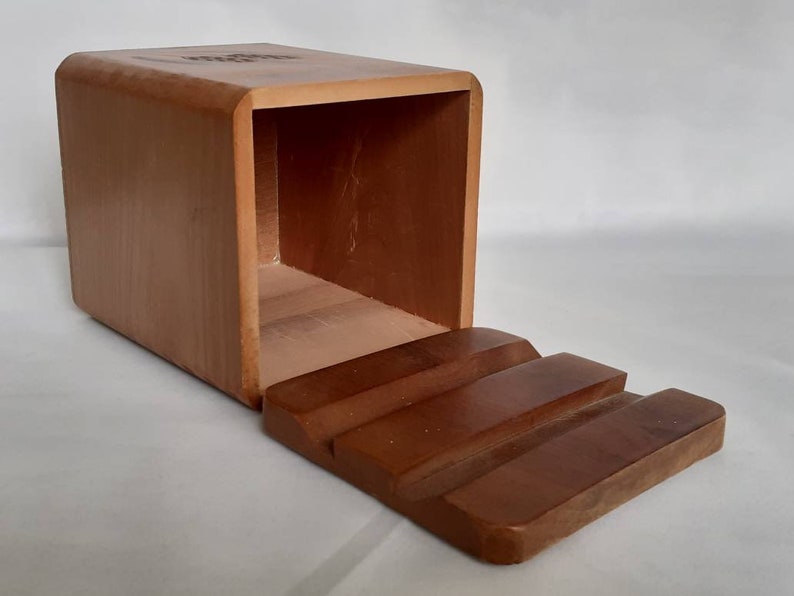 Puede incluir: Una caja rectangular de madera con una parte superior curvada y una tapa con bisagras escalonada. La caja es de color marr&oacute;n claro y la tapa es de un tono marr&oacute;n m&aacute;s oscuro. La caja parece estar vac&iacute;a.