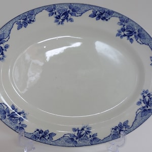 May include: Oval white serving platter with a blue floral border. The border features a repeating pattern of blue roses and decorative scrollwork. The platter is made of ceramic.