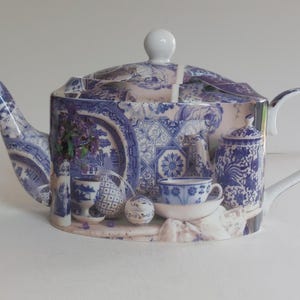 May include: A blue and white porcelain teapot with a detailed design. The teapot features a curved spout, a rounded body, and a white handle. The design includes images of teacups, plates, and floral arrangements. The lid has a white knob.