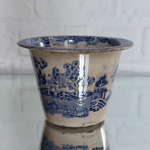 May include: A vintage blue and white ceramic planter with a detailed landscape design. The planter has a wide rim and a slightly flared shape. The blue design is set against a cream-colored background, creating a classic aesthetic.