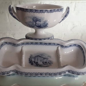 May include: A white porcelain shaving set with blue landscape designs. The set includes a handled cup and a three-section tray. The edges and rims are decorated with a blue floral pattern. The cup is supported by a pedestal.