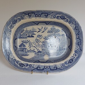 May include: Oval blue and white ceramic platter with a Willow pattern design. The platter features a detailed landscape scene with bridges, pagodas, and birds. The border has a decorative geometric pattern.