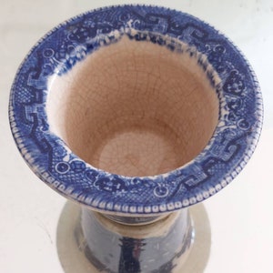 May include: A blue and white ceramic pedestal bowl with a detailed pattern around the rim. The interior is off-white with visible crackling. The base is a light grey colour, and the bowl is set against a white background.
