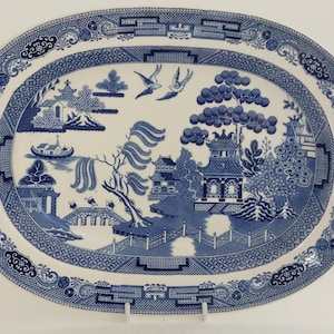 May include: Oval blue and white ceramic platter with a Willow pattern design. The platter features a detailed landscape scene with pagodas, bridges, trees, and birds. The border has a decorative pattern. A classic piece for serving.