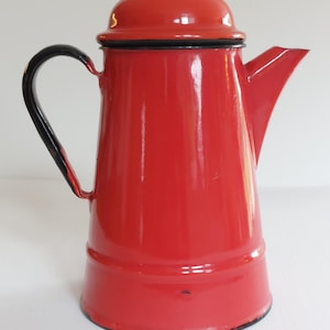 May include: A bright red enamel coffee pot with a black handle and trim. The pot has a lid and a spout for pouring. The vintage kitchenware item is a classic design.