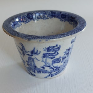 May include: A small, round, white and blue ceramic planter with a detailed Willow pattern. The rim and exterior feature a blue design, while the interior is plain white. The planter has a slightly flared rim and a classic, vintage aesthetic.