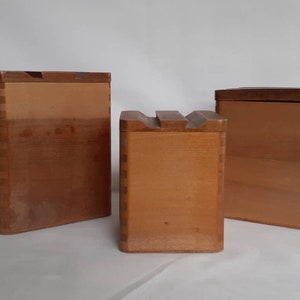 Puede incluir: Tres cajas de madera con tapas. Las cajas son de varios tama&ntilde;os y tienen un color marr&oacute;n claro. Las cajas est&aacute;n construidas con juntas de cola de milano visibles. Las tapas son de un tono marr&oacute;n m&aacute;s oscuro. La caja del medio tiene una parte superior tallada &uacute;nica.