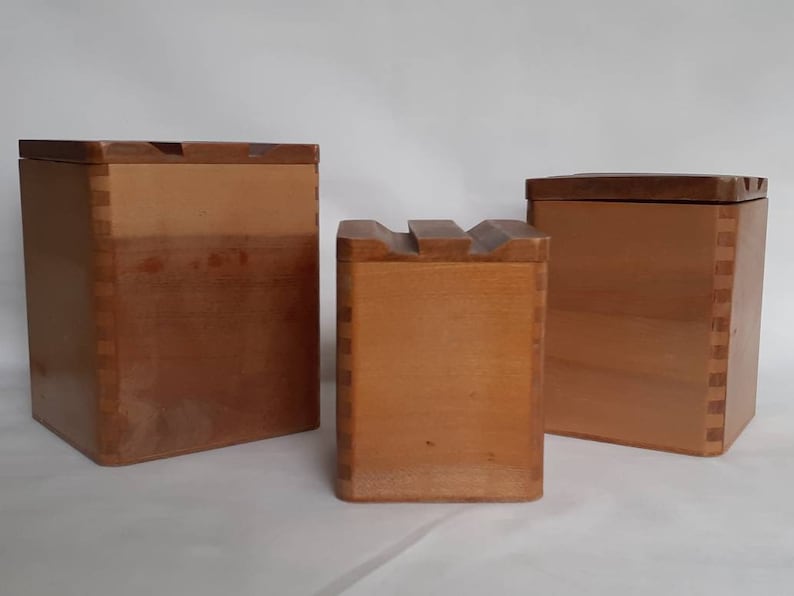Puede incluir: Tres cajas de madera con tapas. Las cajas son de varios tama&ntilde;os y tienen un color marr&oacute;n claro. Las cajas est&aacute;n construidas con juntas de cola de milano visibles. Las tapas son de un tono marr&oacute;n m&aacute;s oscuro. La caja del medio tiene una parte superior tallada &uacute;nica.
