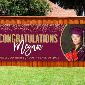 May include: A maroon graduation banner with gold glitter text reading "CONGRATULATIONS Megan" and "EASTWOOD HIGH SCHOOL CLASS OF 2023". A photo of a graduate in a cap and gown is on the right.