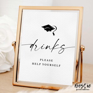 Op de afbeelding: Een gouden lijst met een witte achtergrond en zwarte tekst die "drinks" in een cursief schrift leest. Boven de tekst staat een klein zwart symbool voor een afstudeerpet. Onder de tekst staat "Please help yourself".