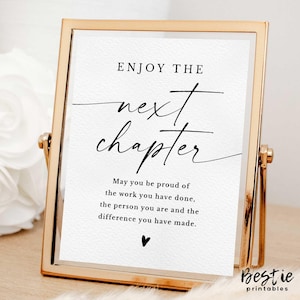 May include: A gold-framed printable sign with the text "ENJOY THE next chapter" in black calligraphy. The sign also includes the text "May you be proud of the work you have done, the person you are and the difference you have made." in black text.