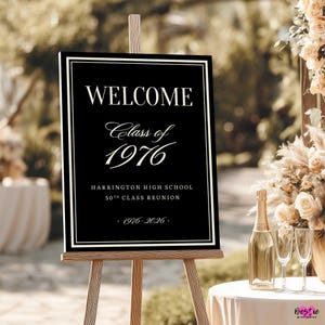 May include: A black rectangular welcome sign on a wooden easel featuring white text that reads WELCOME, Class of 1976, HARRINGTON HIGH SCHOOL 50TH CLASS REUNION, and 1976-2026, framed by a thin white border with a double-line design.