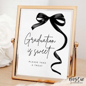 May include: A gold-framed sign with a black ribbon bow and the text "Graduation is sweet. Please take a treat."