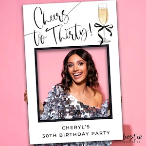 Könnte beinhalten: Ein weißer Fotoautomaten-Requisit mit schwarzem Rahmen und dem Text "Cheers to Thirty!" Ein Glas Champagner mit einer schwarzen Schleife befindet sich oben rechts. Der Text "Cheryl's 30th Birthday Party" befindet sich unten auf dem Requisiten.