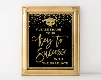 May include: A framed graduation sign with gold glitter text on a black background. The sign reads "PLEASE SHARE YOUR KEY TO SUCCESS WITH THE GRADUATE" and features a graduation cap graphic. The frame is gold.