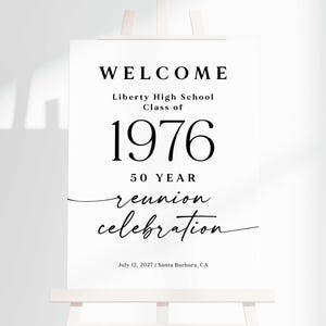 May include: A white rectangular sign with black text that reads WELCOME, Liberty High School Class of 1976, 50 YEAR reunion celebration, and July 12, 2027 | Santa Barbara, CA. The sign is displayed on a light-colored wooden easel stand.