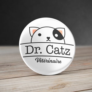 May include: White round button with a black and white cartoon cat with orange ears and the text "Dr. Catz Vétérinaire" in black.
