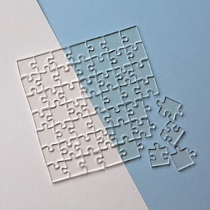 May include: A clear plastic jigsaw puzzle with some pieces removed. The puzzle is on a light blue and pink background.