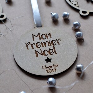 K&ouml;nnte beinhalten: Ein h&ouml;lzerner Weihnachtsbaumschmuck mit dem Text "Mon Premier Noel" und dem Namen "Charlie" sowie dem Jahr "2019" eingraviert. Der Schmuck ist mit einem kleinen Stern verziert und h&auml;ngt an einem wei&szlig;en Band.