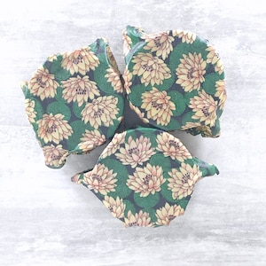 May include: Three reusable food wraps with a floral pattern. The wraps are made of a green and yellow fabric with a floral pattern. The wraps are folded and stacked on top of each other.